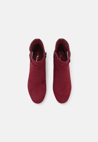 Bottines en suede bourgogne avec une texture lisse, un bout arrondi et un détail de boucle ajustable sur le côté. Vue intérieure de dessus.