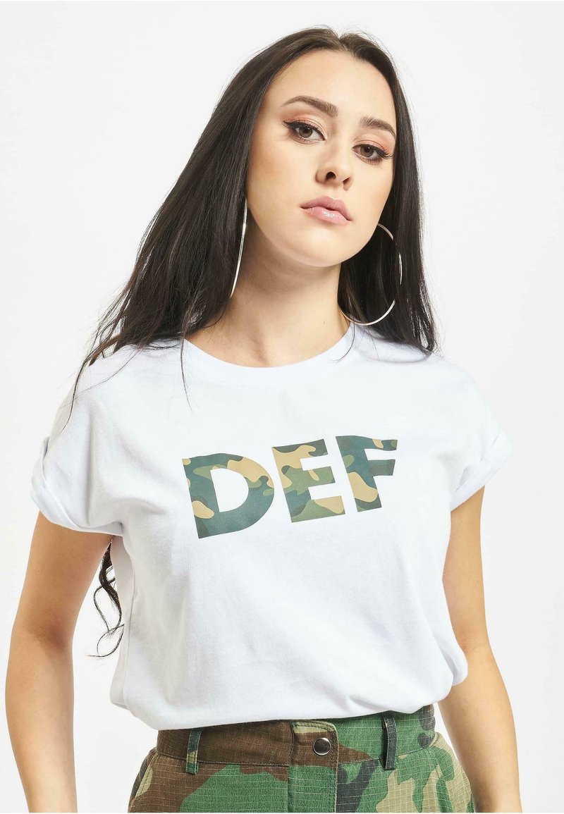 Hvid bomulds t-shirt med op-rullede ærmer, der har store camouflagemønstrede bogstaver, der staver "DEF" i grønne og jordfarver. Model iført olivengrønne bukser.