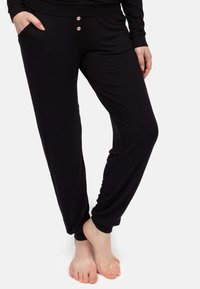 Czarne spodnie dresowe wykonane z miękkiego materiału, charakteryzujące się luźnym krojem, elastycznym pasem i dwoma różowymi guzikami z przodu.