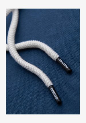 Granatowy materiał z białymi sznurówkami zakończonymi czarnymi metalowymi końcówkami oznaczonymi "DIMARE", pokazujący plecioną fakturę i gładkie wykończenie.