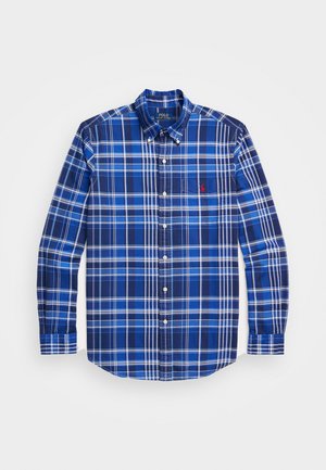 Modrá kostkovaná košile s dlouhým rukávem a límečkem na knoflíky, s různými odstíny modré a bílými pruhy, a malým červeným logem na hrudi.
