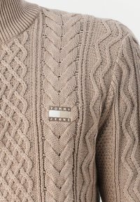 Maglione lavorato a maglia beige con un motivo a treccia testurizzato e colletto a costine. Include un piccolo etichetta con il marchio "TOMMY JEANS".