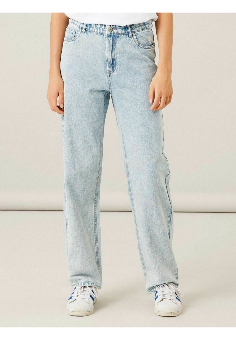 Ljusblå denimjeans med en avslappnad passform, hög midja, fem fickor och subtila blekningar, kombinerade med vita sneakers med blå ränder.