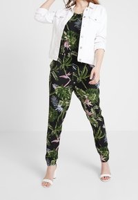 Mono negro con estampado botánico en verde y rosa, combinado con una chaqueta de mezclilla blanca. Presenta un corte relajado y perneras ajustadas; tacones blancos destalonados.