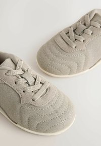 Baskets gris clair en daim avec des coutures texturées et une semelle en caoutchouc lisse. Caractérisées par un design à lacets et une forme à bout rond.
