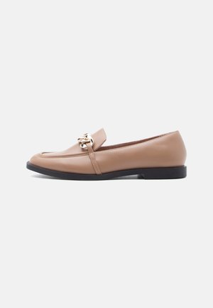 Mocassin plat en cuir beige avec semelle noire et détail chaîne dorée sur le dessus, vue latérale sur fond blanc.