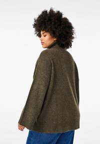Ciemnozielony oversize sweter z wysokim kołnierzem, prążkowanymi mankietami i dołem. Miękka tekstura i luźny krój, w połączeniu z niebieskimi dżinsami.