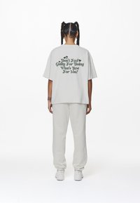 Lös passform ljusgrå t-shirt med mörkgrön text på baksidan som säger "Känn dig inte skyldig för att göra det som är bäst för dig." Enkla vita joggers.