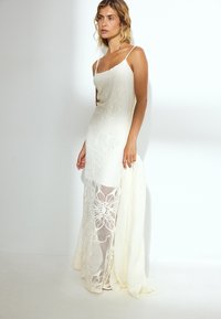 Weißes Kleid mit Spitzenüberzug, floralen Mustern, Spaghettiträgern und einem transparenten unteren Abschnitt. Glatte Textur mit einer fließenden Silhouette.