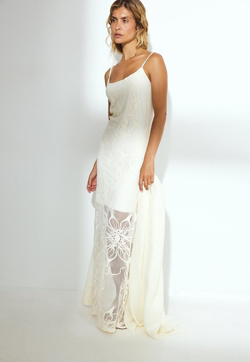 Weißes Kleid mit Spitzenüberzug, floralen Mustern, Spaghettiträgern und einem transparenten unteren Abschnitt. Glatte Textur mit einer fließenden Silhouette.