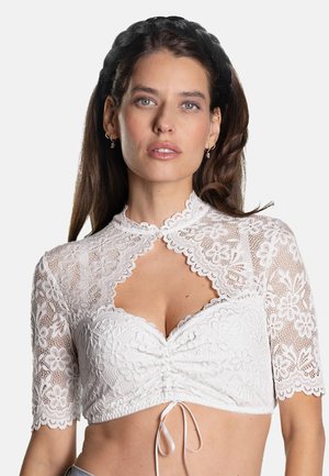 Frau mit langen braunen Haaren trägt ein weißes Spitzen-Crop-Top mit Blumenmuster und kurzen Ärmeln, kombiniert mit einem schwarzen geflochtenen Stirnband.
