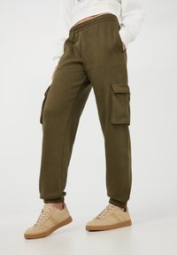 Pantaloni felpa verde oliva con polsini affusolati, vita elastica e tasche laterali cargo. Abbinati a sneakers beige per il massimo comfort.