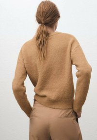 Suéter de punto color canela con una textura suave, que presenta mangas largas y un ajuste relajado, combinado con pantalones marrón claro.