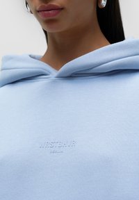 Felpa con cappuccio di colore azzurro chiaro realizzata in tessuto morbido, dotata di cappuccio, logo ricamato "WASTEBNR BERLIN" e cuciture piatte.