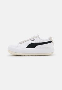 White sneaker with black suede side stripe, beige accents, flat laces, textured rubber sole, and Puma logo on outer side.