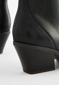 Stivale alla caviglia in pelle nera con finitura strutturata, design affusolato e tacco a cuneo in stile legno scuro, caratterizzato da strisce orizzontali.