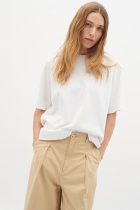 Hvid kortærmet top lavet af blødt materiale, parret med beige, plisserede, højderetede bukser. Simpelt design uden synlige mønstre eller detaljer.