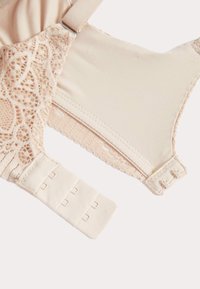 Beige kanten en stoffen bh-sectie met verstelbare schouderband en drievoudige haak-en-oogsluiting aan de achterzijde, op een witte achtergrond.