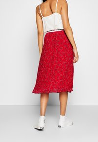 Rote Midi-Rock mit Paisleymuster, leichtem Stoff und elastischem Bund. Kombiniert mit weißen High-Top-Sneakern und einem weißen Tanktop.