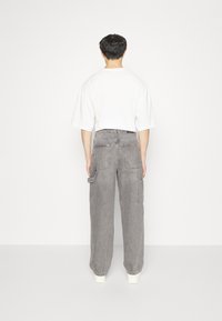 Pantalones cargo de mezclilla gris con un corte holgado, que cuentan con bolsillos laterales y una cintura de altura media, combinados con una camiseta blanca relajada.