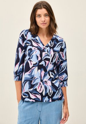 Chemise à motif floral bleu marine, présentant des teintes de bleu et de rose, avec des manches courtes à poignets froncés et un décolleté en V. Tissu léger.