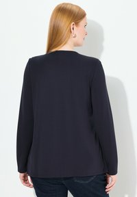 Marineblauw longsleeve top met een ronde halslijn, een gladde textuur en een relaxte pasvorm, gecombineerd met donkere spijkerbroek.