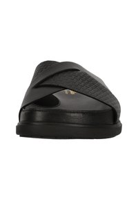 Svart slip-on sandal med flätad ovandel, med en texturerad yta, öppen tå och en platt gummisula. Enkel och modern estetik.