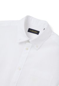 Camisa blanca de botones hecha de algodón, con cuello puntiagudo, un bolsillo en el pecho y detalles de costura visibles. La etiqueta dice "PIOMBO."
