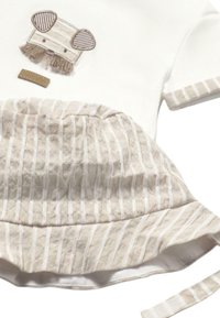 Camisa de algodón blanca con un diseño de animal bordado en marrón, combinada con un sombrero de cubo de algodón a rayas beige con una textura deshilachada.
