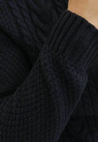 Dunkelblauer gestrickter Pullover mit einem strukturierten Muster und Zopfmuster. Der Ärmel hat einen gerippten Bündchen. Das Material wirkt weich und dick.