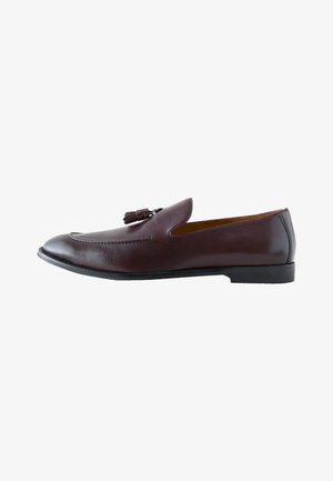 Mocassino da uomo in pelle marrone con dettaglio nappine, tacco basso nero e bordo cucito lungo il bordo superiore.
