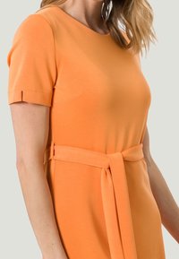 Pomarańczowa sukienka z krótkim rękawem, wykonana z gładkiego materiału; posiada pasek w talii, okrągły dekolt oraz subtelny rozporek po boku rękawów.