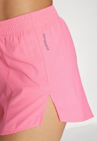 Shorts atletici roz cu un brâu elastic prezintă o fanta laterală pentru un plus de libertate de mișcare. Materialul este ușor și fin, marcat cu "AEROREADY."