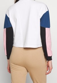 Gekürzter Sweatshirt mit Farbkombinationen in Weiß, Marineblau, Schwarz, Pink und Blau; aus Baumwolle gefertigt, mit langen Ärmeln und gerippten Bündchen.