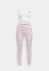 Crop top blanc avec une application de cerise, associé à des leggings blancs ornés d'un motif répétitif de cerises. Les deux sont en tissu doux.