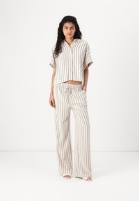 Ensemble en lin comprenant une chemise à col et manches courtes ainsi qu'un pantalon à jambes larges. Tissu blanc cassé avec des rayures verticales bleu marine, comportant une taille élastique à cordon.