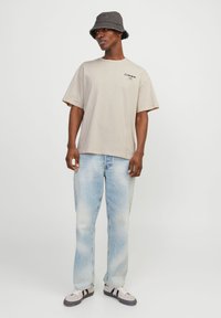 T-shirt en coton beige avec un col rond et des manches courtes, associé à un jean en denim bleu clair. Des baskets avec des accents noirs complètent la tenue.