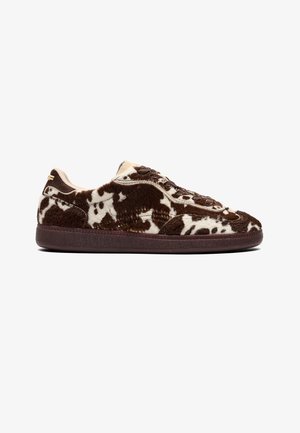 Low-top sneaker met een bruin-wit koeienhuidpatroon, gestructureerd bovenwerk, donkerbruine zool en afgeronde neus, zijaanzicht.