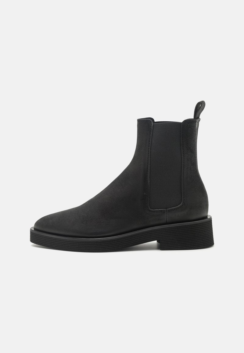 Botte Chelsea en cuir noir avec panneaux latéraux élastiques, talon bloc bas, bout arrondi et languette à l'arrière.