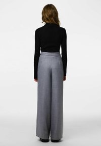 Szare, wysokowaistowe spodnie z szerokimi nogawkami, wykonane z teksturowanej tkaniny. Z tyłu widoczny jest przymocowany czarny golf z prążkowanego materiału.