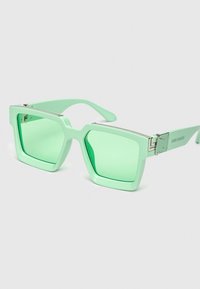 Gafas de sol cuadradas de color verde menta con montura transparente, lentes tintados en verde y acentos metálicos en las bisagras. Diseño moderno y geométrico.