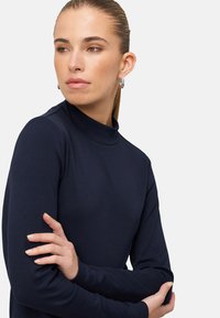 Tmavě modrý rolák z měkké látky, s dlouhými rukávy a přiléhavým střihem. Hladká textura s minimalistickým stylem.