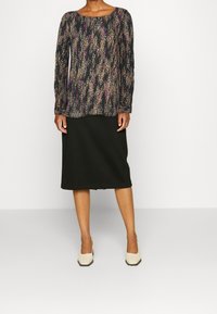 Blusa a maniche lunghe con un motivo astratto multicolore su sfondo nero. Abbinata a una gonna nera a metà coscia e tacchi beige.