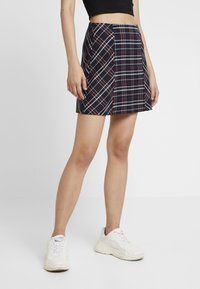 Jupe mini à carreaux en bleu marine, rouge et blanc. Présente un design ajusté avec des plis et un ourlet droit. Associée à des baskets blanches.