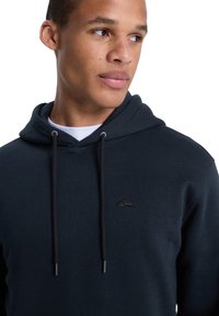 Navy hooded sweatshirt in soft fabric with a front kangaroo pocket. Features a small black logo on the chest and drawstring accents.