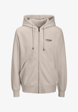 Sudadera con capucha beige claro con cremallera, capucha con cordón, bolsillos delanteros, puños acanalados y logo negro "JJ Studios" en el pecho izquierdo. Tejido suave.
