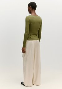 Olivenfarbene Rippstrick-Langarmbluse kombiniert mit lockeren, cremfarbenen Hosen. Die Bluse hat einen runden Halsausschnitt, eine glatte Stofftextur und eine figurnahe Silhouette.