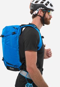 Blauer, strukturierter Rucksack mit hexagonalem Muster, verstellbaren Trägern und Millet-Logo. Getragen von einer Person in einem schwarzen T-Shirt und Helm.