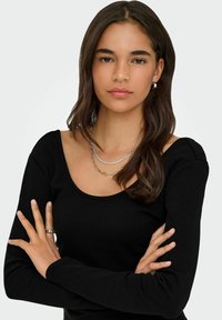 Sort langærmet top med bred udskæring, glat tekstur og tætsiddende design. Modellen bærer lagdelte sølvringe og en ring.