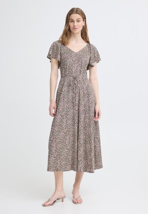 Naine kannab roosa ja musta leopardimustriga midi-kleit, lühikeste lendlevate varrukatega, V-kaelusega ja kergesti jalga tõmmatavate kontsadega sandaalidega.